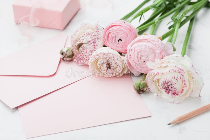 Envelope or letter, paper card, gift and pink ranunculus flowers on white table for greeting on Mother or Woman Day.