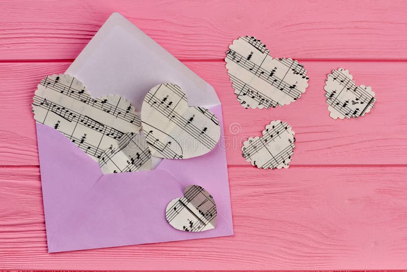 Envelope and paper hearts with music notes. Opened colorful envelope and paper hearts, top view. Love letter concept.