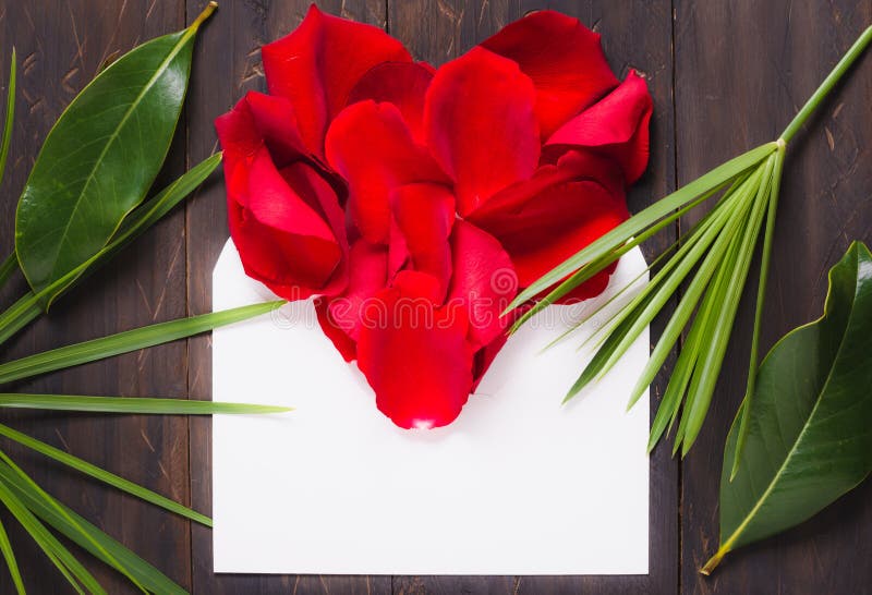 Envelope with text space on wood background flat lay and red rose petals heart. Letter valentine card.