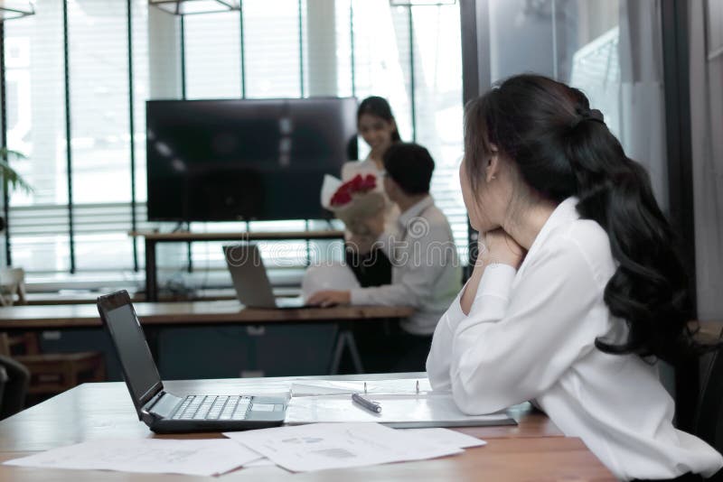 Envious angry Asian business women looking affectionate couple in love in office. Jealousy and envy in friend relationship .