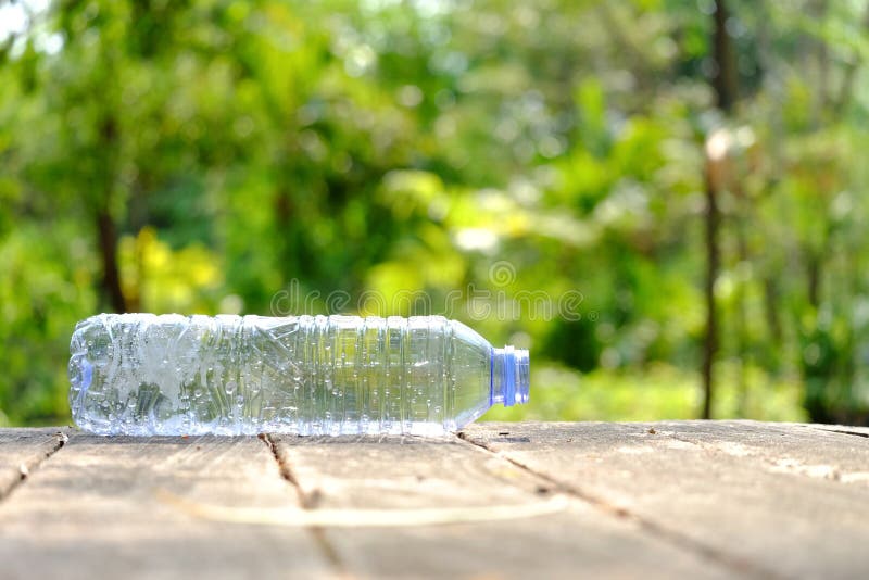 A plastic bottle of drinking water littering on the old wood table at the public park with green nature and sunlight background stock images A plastic bottle of drinking water littering on the old wood table at the public park with green nature and sunlight background stock images