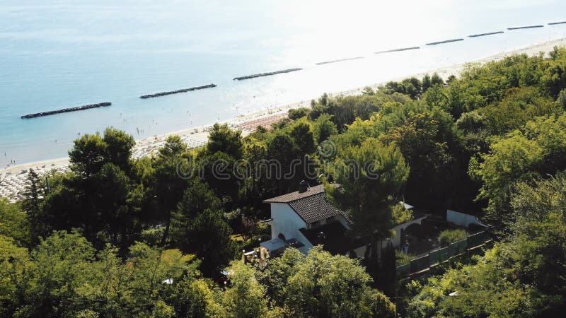 Epic Anial shot di una casa su Green Tree Hill con una straordinaria vista della spiaggia estiva del Mediterraneo a Pesaro, Itali