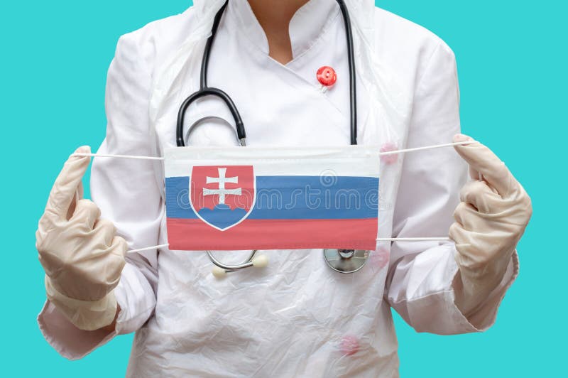 Epidemic in Slovakia. Young woman doctor in a medical coat and gloves holds a medical mask with the print of the flag of Slovakia