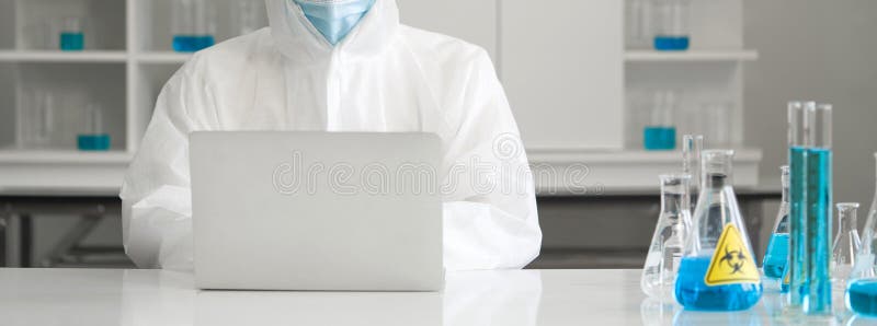 Epidemiological researcher in virus protective cloth typing on laptop computer in laboratory. Omicron strain testing process stock image