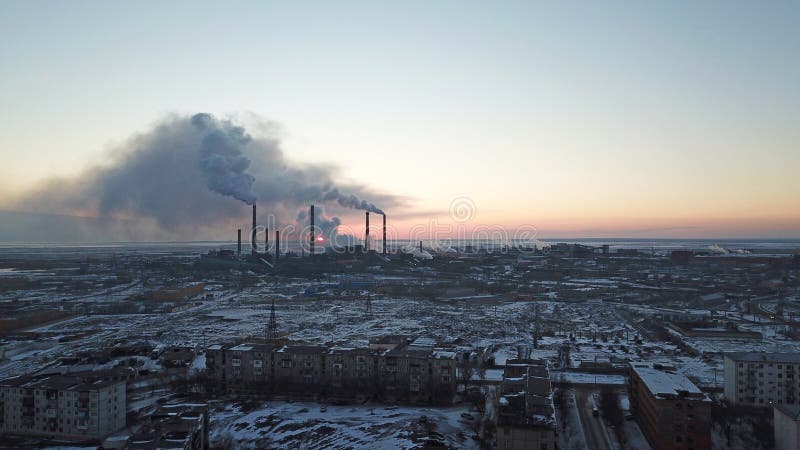 Episk solnedgång på bakgrunden av en röka fabrik Den röda solen med ljusa strålar går utöver den rörfabrikerna och smogen arkivbild Episk solnedgång på bakgrunden av en röka fabrik Den röda solen med ljusa strålar går utöver den rörfabrikerna och smogen arkivbild