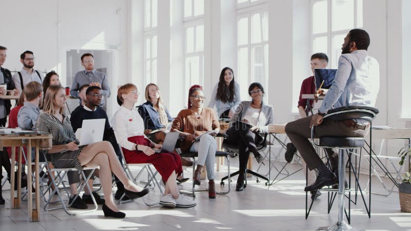 Episódios vermelhos, jovens e felizes empresário negro, fazendo um discurso para a equipe de gerentes multiétnicos em movimento le