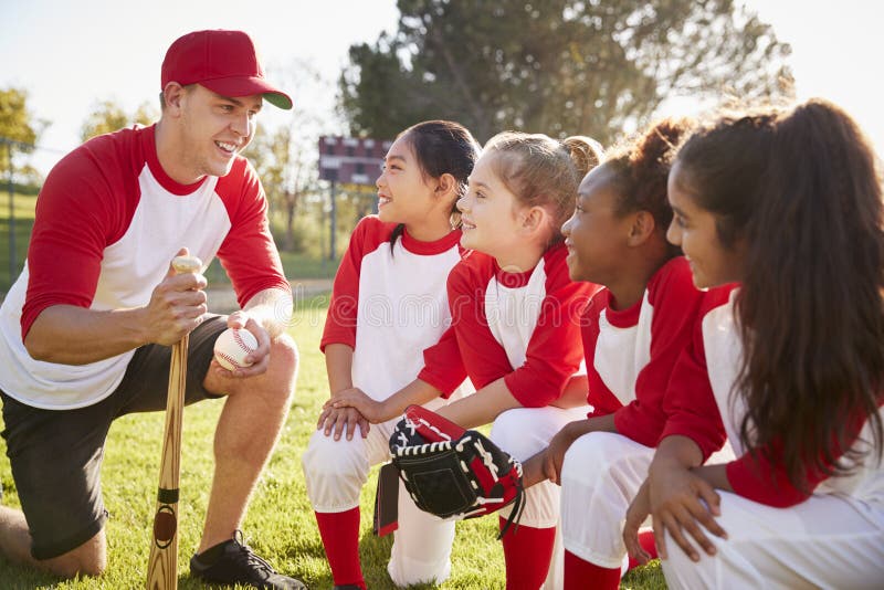 Equipa de beisebol da menina que ajoelha-se em uma aproximação com seu treinador