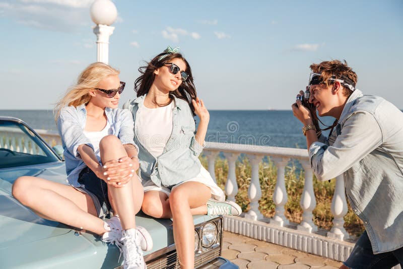 Equipaggi il fotografo che prende le foto di due donne che si siedono sull'automobile fotografie stock libere da diritti Equipaggi il fotografo che prende le foto di due donne che si siedono sull'automobile fotografie stock libere da diritti