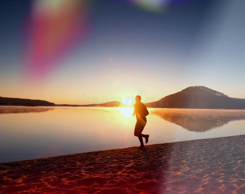 Equipaggi il funzionamento sulla spiaggia contro il contesto di bello tramonto Sabbia del lago della montagna fotografia stock Equipaggi il funzionamento sulla spiaggia contro il contesto di bello tramonto Sabbia del lago della montagna fotografia stock