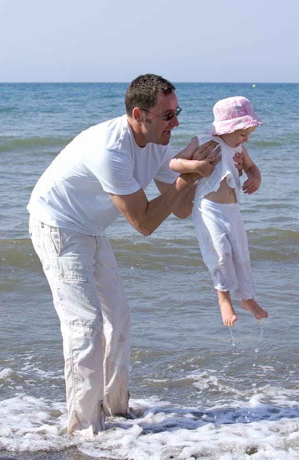 Equipaggi il sollevamento della sua figlia ed il gioco nel mare fotografia stock