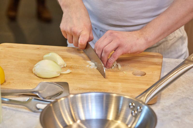 Equipaggi il taglio della cipolla con il coltello sul bordo di legno immagine stock Equipaggi il taglio della cipolla con il coltello sul bordo di legno immagine stock