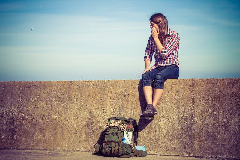 Equipaggi il viaggiatore con zaino e sacco a pelo turistico che si siede sulla parete di lerciume all'aperto fotografia stock libera da diritti Equipaggi il viaggiatore con zaino e sacco a pelo turistico che si siede sulla parete di lerciume all'aperto fotografia stock libera da diritti