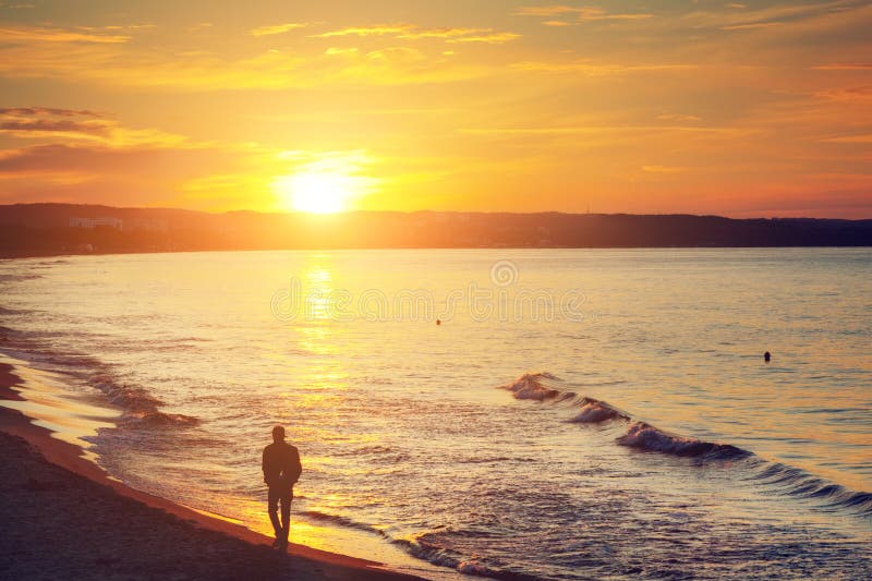 Equipaggi la camminata da solo sulla spiaggia al tramonto Mare calmo fotografia stock libera da diritti Equipaggi la camminata da solo sulla spiaggia al tramonto Mare calmo fotografia stock libera da diritti