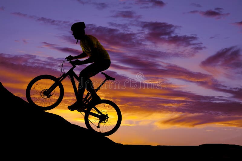 Equipaggi la guida della bici su una siluetta della collina nel tramonto