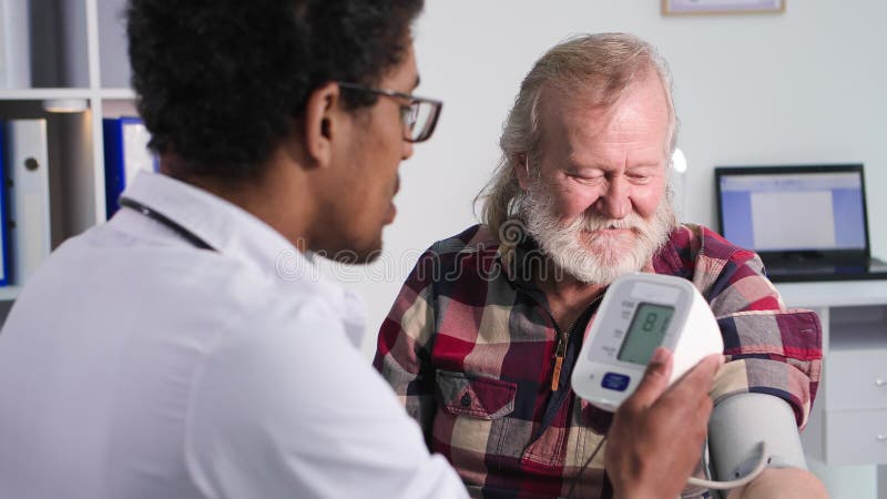 Equipamento médico moderno um jovem médico negro profissional mede a pressão de um idoso durante um tratamento médico