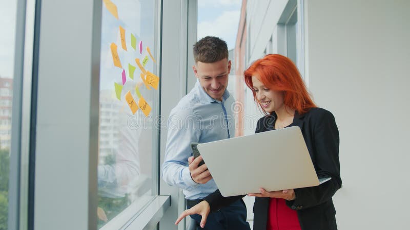 Equipe de dois jovens parceiros de negócios discutindo orientações estratégicas de negócios conversando ao telefone em um laptop