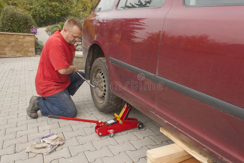 Equipe a mudança do pneumático puncionado em seu carro que afrouxa as porcas com uma chave inglesa da roda antes de levantar acim imagens de stock Equipe a mudança do pneumático puncionado em seu carro que afrouxa as porcas com uma chave inglesa da roda antes de levantar acim imagens de stock