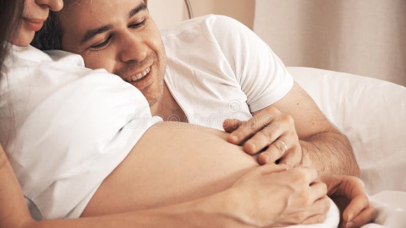 Equipe o afago da barriga grávida do ` s da esposa na cama em casa
