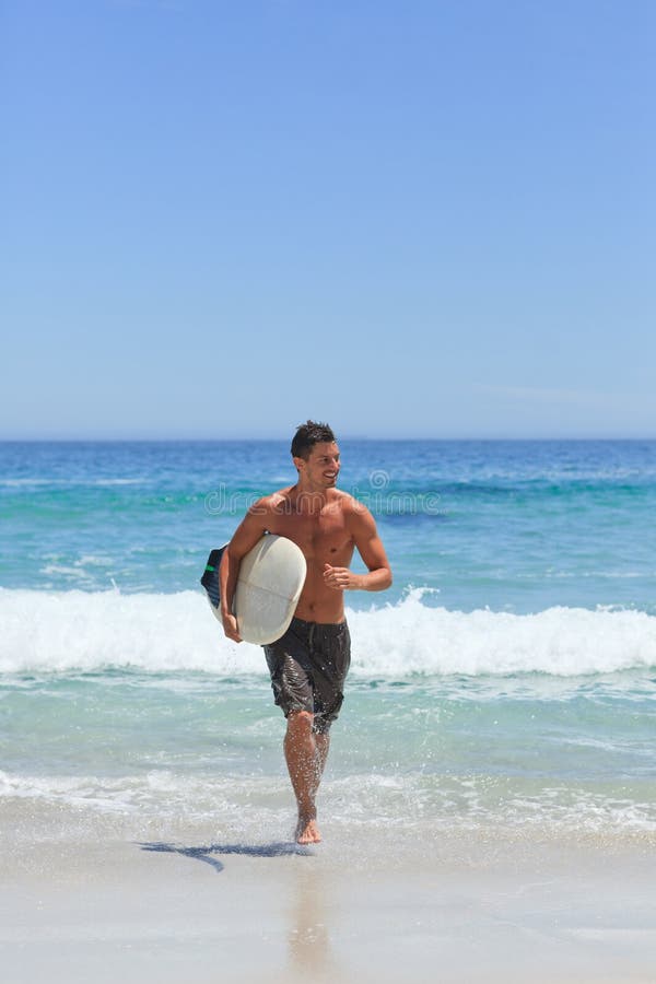 Homem a correr na praia com a sua prancha de surf foto de stock