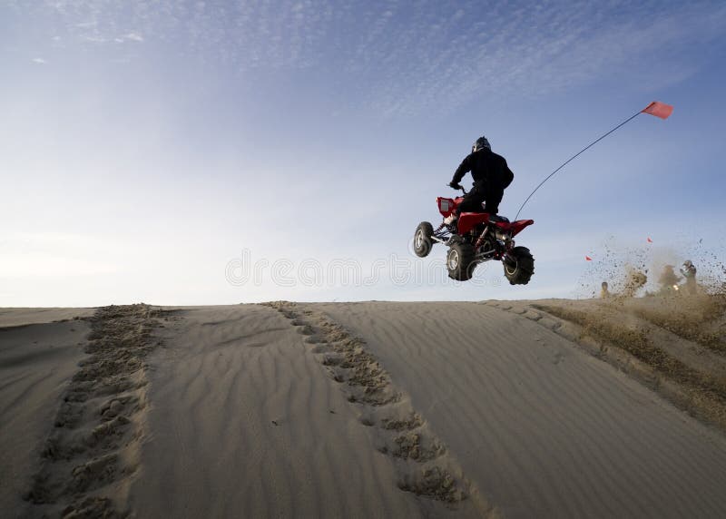 Evening shot of a man in safety gear jumping his quadbike over a sand dune. Good space for ad copy. Evening shot of a man in safety gear jumping his quadbike over a sand dune. Good space for ad copy.