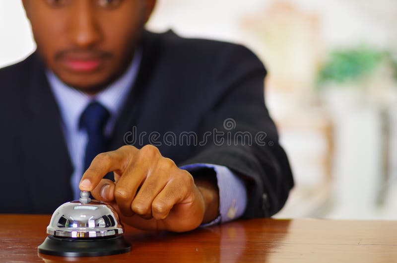 Equipe o terno azul elegante vestindo que pressiona o sino da mesa na recepção do hotel foto de stock Equipe o terno azul elegante vestindo que pressiona o sino da mesa na recepção do hotel foto de stock