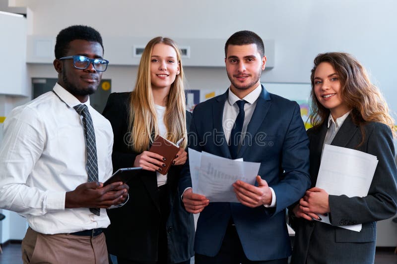 Multiethnic team of corporate professionals gather, smiling African, Caucasian woman, Arabic man, Asian businesswoman in office setting, engaged in strategy session displaying partnership. Multiethnic team of corporate professionals gather, smiling African, Caucasian woman, Arabic man, Asian businesswoman in office setting, engaged in strategy session displaying partnership.