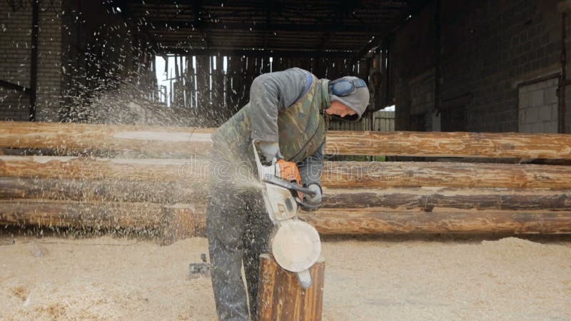 Erbauer behandelt hölzerne Bauholzkettensäge Gegen den Hintergrund ist ein Teil der Zukunft des Hauses, das von den Holzbalken ge
