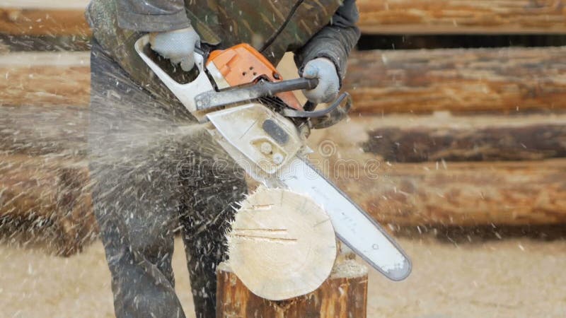 Erbauer behandelt hölzerne Bauholzkettensäge Gegen den Hintergrund ist ein Teil der Zukunft des Hauses, das von den Holzbalken ge