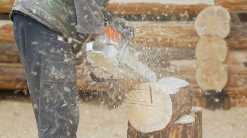 Erbauer behandelt hölzerne Bauholzkettensäge Gegen den Hintergrund ist ein Teil der Zukunft des Hauses, das von den Holzbalken ge