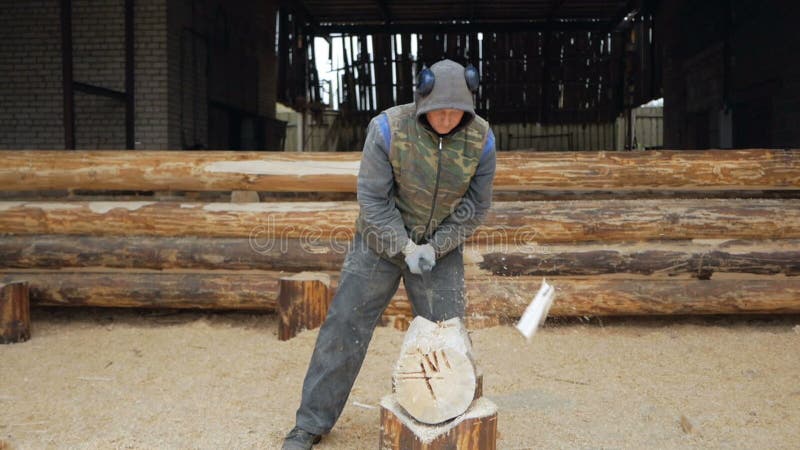 Erbauer behandelt hölzernes Bauholz mit Axt Gegen den Hintergrund ist ein Teil der Zukunft des Hauses, das von den Holzbalken gem