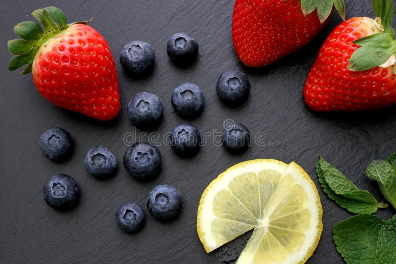 Erdbeeren, Zitronenscheiben, tadellose Blätter und Blaubeeren auf schwarzem Schieferhintergrund stockfoto Erdbeeren, Zitronenscheiben, tadellose Blätter und Blaubeeren auf schwarzem Schieferhintergrund stockfoto