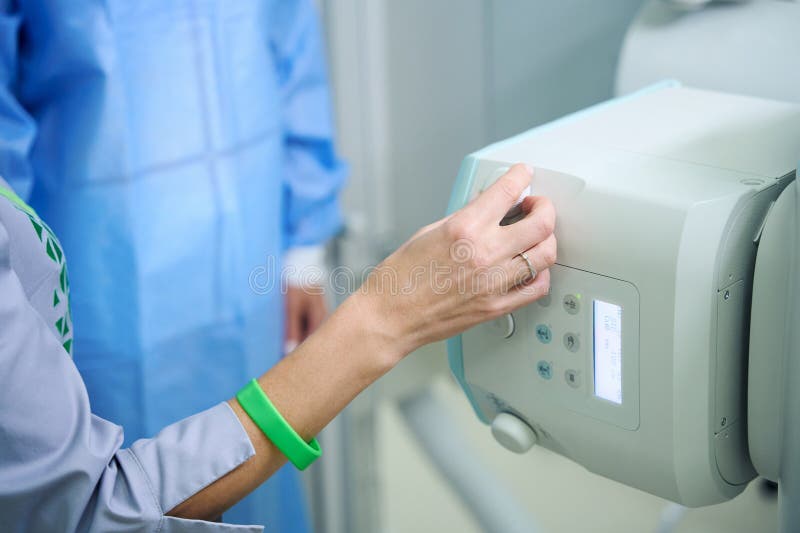 Cropped photo of radiologic technologist adjusting x-ray tube in front of gowned patient. Cropped photo of radiologic technologist adjusting x-ray tube in front of gowned patient