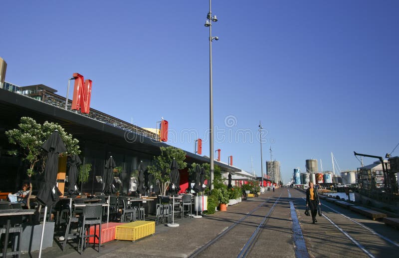 Modification of repository restored into sightseeing destination in North Wharf, Wynyard Quarter, Auckland, New Zealand. Redevelopment of cargo storehouse converted into restaurants with outdoor seating, and abandoned train rails on pedestrian boardwalk. Transformation of old building redeveloped into eateries with exterior seats and tables, and decommissioned rail tracks on promenade. Remodeling of dockside depository transformed into cafes with outside chairs and stools, and railroad tracks on pathway. Conversion of freight depot rebuilt into popular tourist attraction in docklands. Restoration of storage architecture renovated into bars. Rebuilding of architectural landmark modified into dinning. road street path walk passage passageway. Modification of repository restored into sightseeing destination in North Wharf, Wynyard Quarter, Auckland, New Zealand. Redevelopment of cargo storehouse converted into restaurants with outdoor seating, and abandoned train rails on pedestrian boardwalk. Transformation of old building redeveloped into eateries with exterior seats and tables, and decommissioned rail tracks on promenade. Remodeling of dockside depository transformed into cafes with outside chairs and stools, and railroad tracks on pathway. Conversion of freight depot rebuilt into popular tourist attraction in docklands. Restoration of storage architecture renovated into bars. Rebuilding of architectural landmark modified into dinning. road street path walk passage passageway