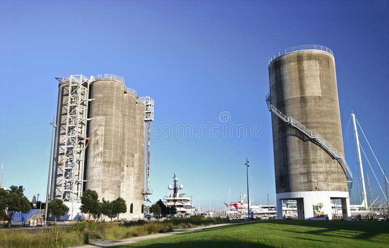 Redevelopment of gray concrete gas and oil silos converted into urban landscape, and sailboats in harbour in New Zealand. Modification of decommissioned grey cylindrical repository towers restored into sightseeing destination, and sailing boats in marina. Transformation of storage tank architecture on brownfield redeveloped into recreation park, and ships in harbor. Remodeling of dockside depository tanks transformed into popular tourist attraction. Conversion of tower structures in industrial area remodeled into city garden. Restoration of old circular storehouse buildings renovated into architectural landmark. Redevelopment of gray concrete gas and oil silos converted into urban landscape, and sailboats in harbour in New Zealand. Modification of decommissioned grey cylindrical repository towers restored into sightseeing destination, and sailing boats in marina. Transformation of storage tank architecture on brownfield redeveloped into recreation park, and ships in harbor. Remodeling of dockside depository tanks transformed into popular tourist attraction. Conversion of tower structures in industrial area remodeled into city garden. Restoration of old circular storehouse buildings renovated into architectural landmark.