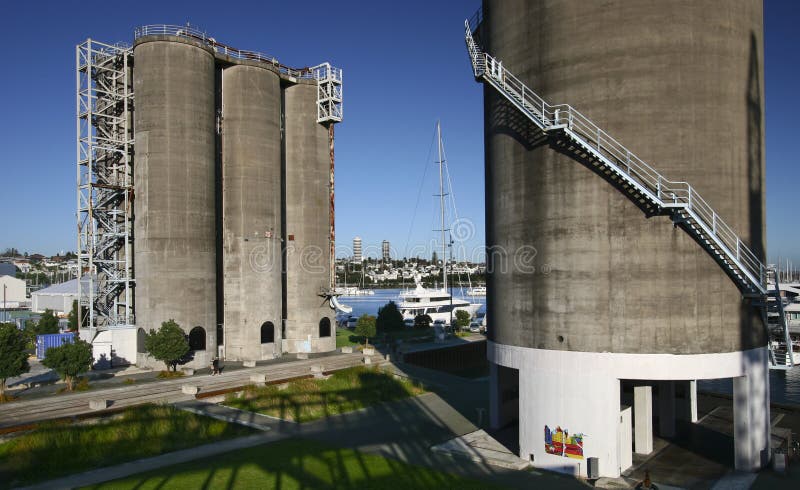 Redevelopment of gray concrete gas and oil silos converted into urban landscape, and sailboats in harbour in New Zealand. Modification of decommissioned grey cylindrical repository towers restored into sightseeing destination, and sailing boats in marina. Transformation of storage tank architecture on brownfield redeveloped into recreation park, and ships in harbor. Remodeling of dockside depository tanks transformed into popular tourist attraction. Conversion of tower structures in industrial area remodeled into city garden. Restoration of old circular storehouse buildings renovated into architectural landmark. Redevelopment of gray concrete gas and oil silos converted into urban landscape, and sailboats in harbour in New Zealand. Modification of decommissioned grey cylindrical repository towers restored into sightseeing destination, and sailing boats in marina. Transformation of storage tank architecture on brownfield redeveloped into recreation park, and ships in harbor. Remodeling of dockside depository tanks transformed into popular tourist attraction. Conversion of tower structures in industrial area remodeled into city garden. Restoration of old circular storehouse buildings renovated into architectural landmark.