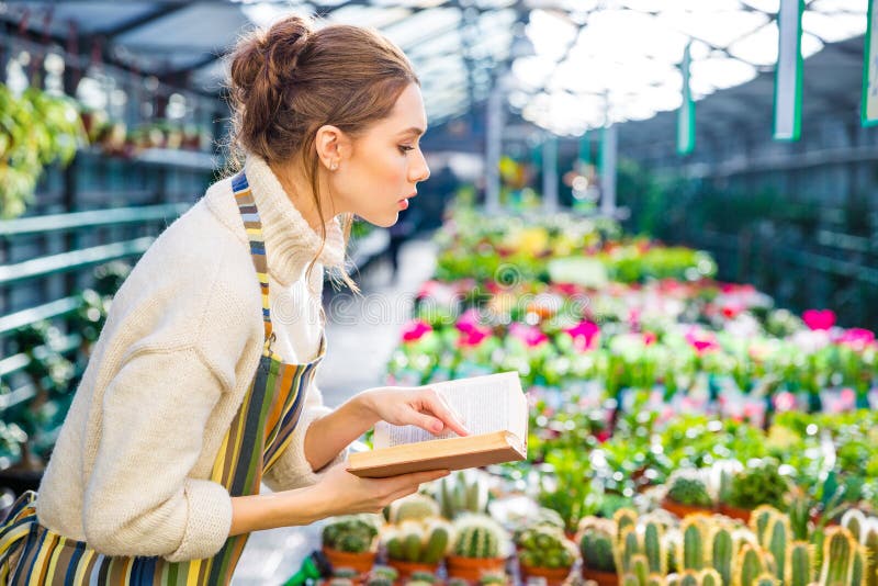 Ernste Frau mit dem Buch, das in Garten-Center arbeitet lizenzfreie stockbilder Ernste Frau mit dem Buch, das in Garten-Center arbeitet lizenzfreie stockbilder