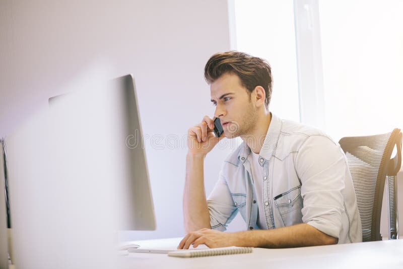 Ernster Mann, der am Handy bei der Anwendung der Laptop-Computers am Schreibtisch in der Studie spricht lizenzfreies stockbild Ernster Mann, der am Handy bei der Anwendung der Laptop-Computers am Schreibtisch in der Studie spricht lizenzfreies stockbild