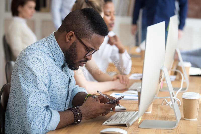 Ernstige Afrikaanse Amerikaanse mens die smartphone gebruiken op het werk stock afbeelding Ernstige Afrikaanse Amerikaanse mens die smartphone gebruiken op het werk stock afbeelding