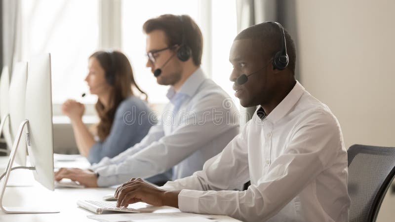 Ernstige Afrikaanse call centreagent in hoofdtelefoon die aan computer werken