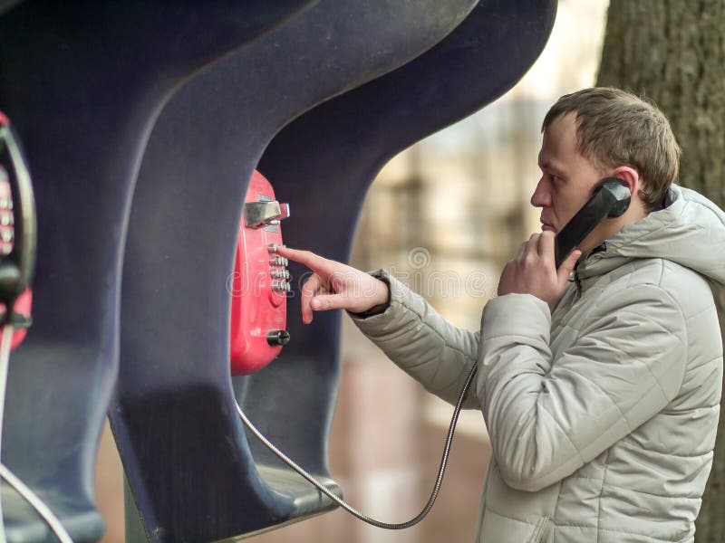 Ernstige jonge mens die door rode straatpayphone roepen stock foto's Ernstige jonge mens die door rode straatpayphone roepen stock foto's