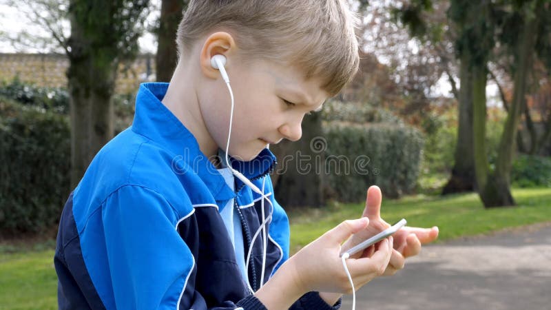 Ernstige tienerjongen met smartphone die of in Brits park luisteren spreken tiener en sociaal media concept stock fotografie Ernstige tienerjongen met smartphone die of in Brits park luisteren spreken tiener en sociaal media concept stock fotografie
