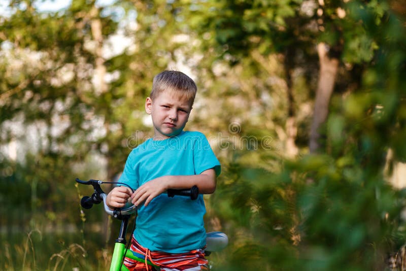 Ernstige zeven-jaar-oude jongen op een fiets die de camera op een vage natuurlijke achtergrond bekijken royalty-vrije stock afbeeldingen Ernstige zeven-jaar-oude jongen op een fiets die de camera op een vage natuurlijke achtergrond bekijken royalty-vrije stock afbeeldingen