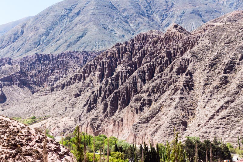 Purmamarca kullar av flera färger bland som är förhärskande rött, violett, purpurfärgat, rosa, orange, brunt Eroderade berg i argentinaren Anderna och grön vegetation