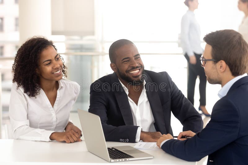 Excited african American couple talk with male realtor or broker consult buying first home together, smiling black husband and wife speak with banker or lawyer discuss taking loan or mortgage. Excited african American couple talk with male realtor or broker consult buying first home together, smiling black husband and wife speak with banker or lawyer discuss taking loan or mortgage