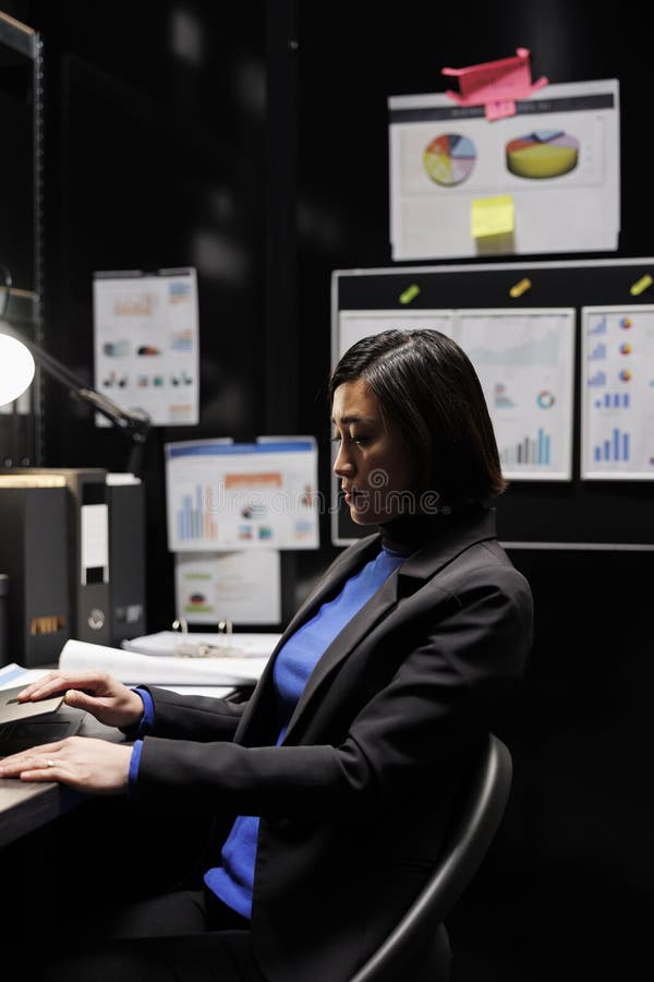 Tired accountancy asian employee in storage room office clocking out from work after long day, shutting down laptop. Bookkeeper executive in archival depository surrounded by folders and flowcharts. Tired accountancy asian employee in storage room office clocking out from work after long day, shutting down laptop. Bookkeeper executive in archival depository surrounded by folders and flowcharts