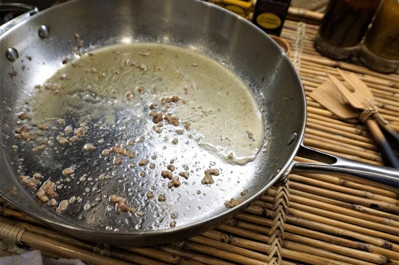 Bits of sausage and beef meat and liquid grease sit cooling in a metal frying pan on a bamboo tray. Wooden kitchen cooking instruments like a fork and spatula rest beside the dirty fry skillet. Bits of sausage and beef meat and liquid grease sit cooling in a metal frying pan on a bamboo tray. Wooden kitchen cooking instruments like a fork and spatula rest beside the dirty fry skillet.