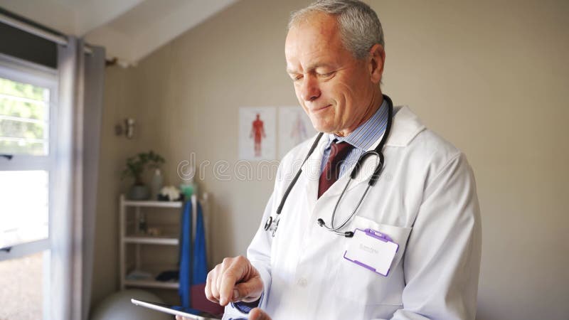 Ervaren arts die op zoek is naar testresultaten van patiënten die digitale tablet in de kliniek houden.