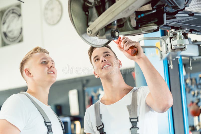 Ervaren autowerktuigkundige die een leerling over schijfremmen onderwijzen stock foto's Ervaren autowerktuigkundige die een leerling over schijfremmen onderwijzen stock foto's