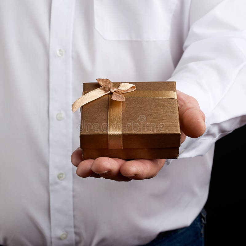 Erwachsene in einem weißen Hemd halten in der Hand eine quadratische kleine Box mit einem Bogen stockfoto
