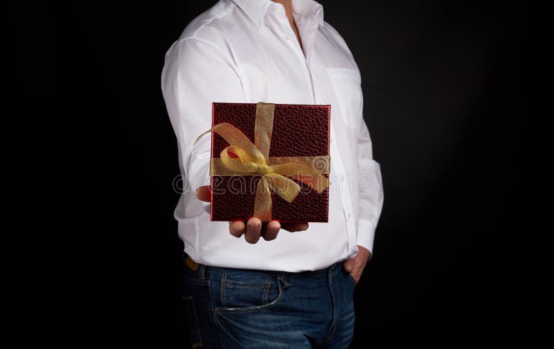 Erwachsene in einem weißen Hemd halten eine rote quadratische Box mit einem geknüpften goldenen Bug stockfotos